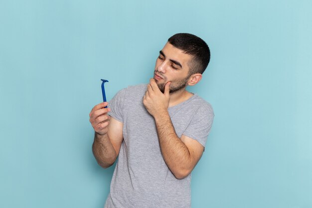 Vista frontal del hombre joven en camiseta gris sosteniendo la navaja y pensando en el azul