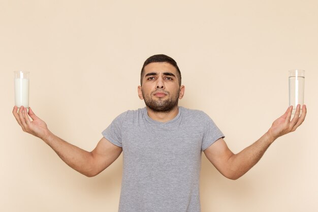 Vista frontal hombre joven en camiseta gris con vaso de agua, leche en beige