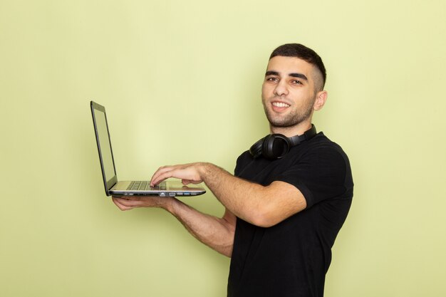 Vista frontal del hombre joven en camiseta negra sonriendo y usando la computadora portátil en verde