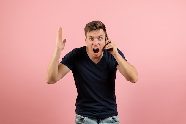 Vista frontal del hombre joven en camiseta oscura hablando por teléfono sobre fondo rosa