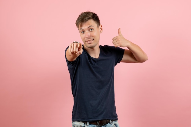 Vista frontal del hombre joven en camiseta oscura y jeans apuntando sobre fondo rosa