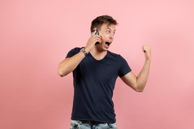 Vista frontal del hombre joven en camiseta oscura y jeans hablando por teléfono sobre fondo rosa