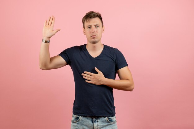 Vista frontal del hombre joven en camiseta oscura y jeans mostrando su mano sobre fondo rosa