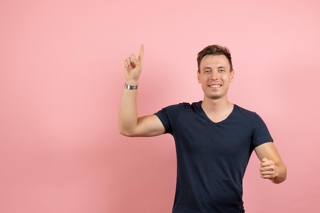Vista frontal del hombre joven en camiseta oscura levantando el dedo sobre fondo rosa