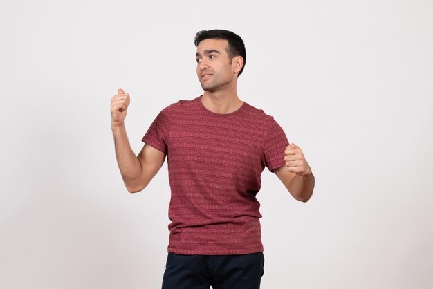 Vista frontal del hombre joven en camiseta de pie y posando en el escritorio blanco