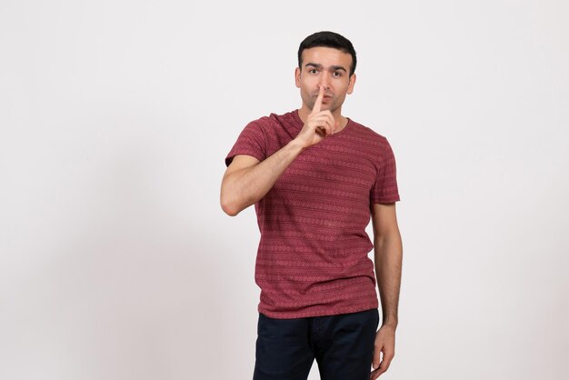 Vista frontal del hombre joven en camiseta roja oscura posando en el escritorio blanco