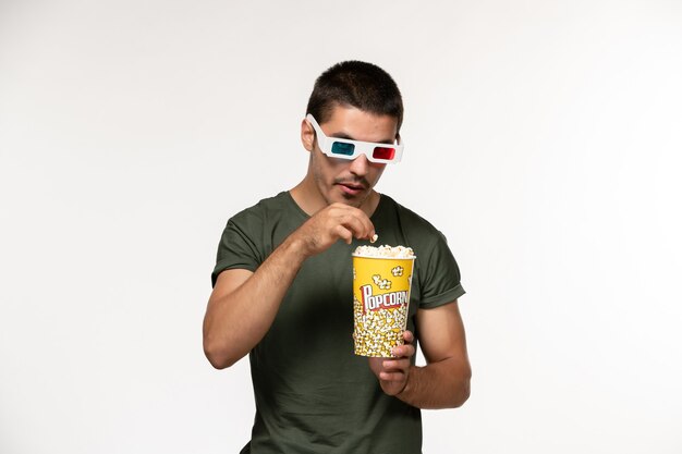 Vista frontal hombre joven en camiseta verde con palomitas de maíz en gafas de sol d en película de pared blanca películas masculinas de cine solitario