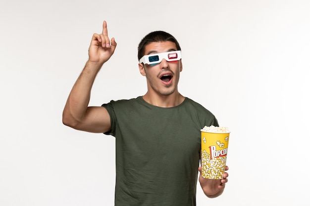 Vista frontal hombre joven en camiseta verde con palomitas de maíz en gafas de sol d viendo la película en la pared blanca película película masculina de cine solitario