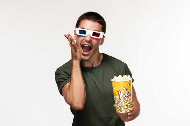 Vista frontal hombre joven en camiseta verde con paquete de palomitas de maíz en gafas de sol d en película de pared blanca clara película masculina de cine solitario