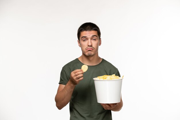 Vista frontal hombre joven en camiseta verde con patatas cips y comiendo en la pared blanca persona película solitaria película cine