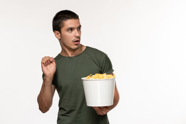 Vista frontal hombre joven en camiseta verde con patatas cips viendo la película en la pared de color blanco claro película persona hombre cine películas solitarias