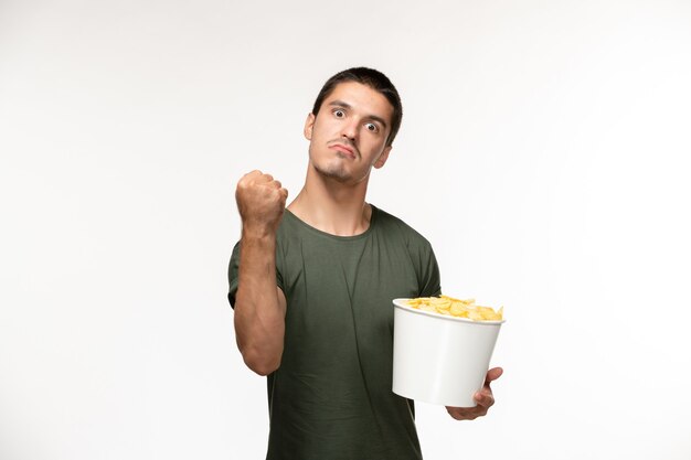 Vista frontal hombre joven en camiseta verde con patatas fritas y amenazando en la pared blanca película persona películas solitarias cine