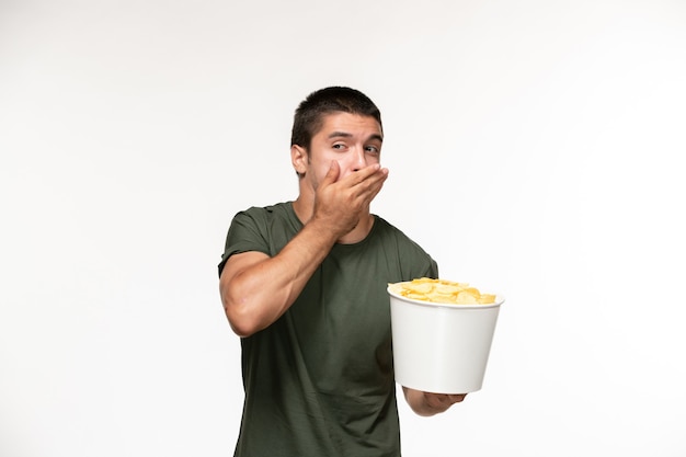 Vista frontal del hombre joven en camiseta verde con patatas fritas en la pared blanca película película cine persona