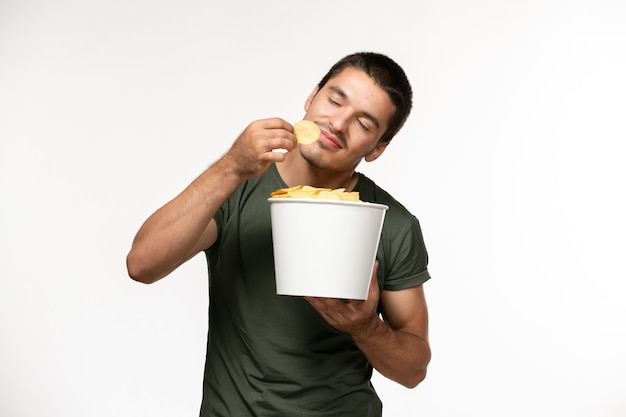 Vista frontal del hombre joven en camiseta verde sosteniendo cips de patata comiendo en la pared blanca película solitaria película persona de cine