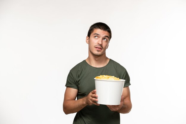 Vista frontal del hombre joven en camiseta verde sosteniendo cips de patata y pensando en la pared blanca película solitaria películas cine persona