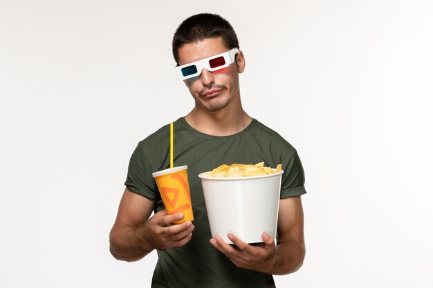 Vista frontal hombre joven en camiseta verde sosteniendo cips de patata y soda en d gafas de sol en la película de escritorio blanco masculino película solitaria