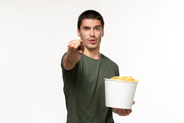 Vista frontal del hombre joven en camiseta verde sosteniendo cips de patata y viendo la película en la pared blanca clara película solitaria película cine