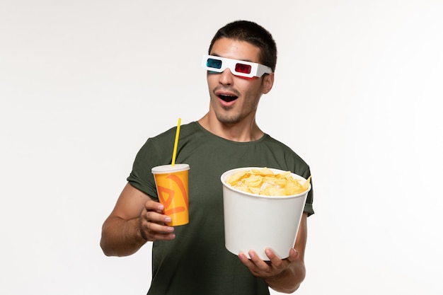 Vista frontal hombre joven en camiseta verde sosteniendo soda cips de patata en -d gafas de sol en la pared blanca película masculina película solitaria