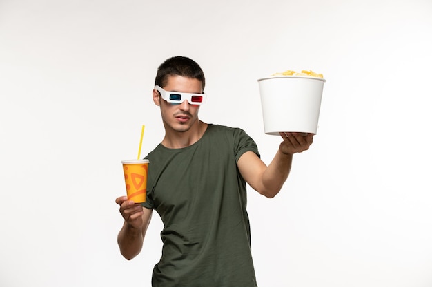 Vista frontal hombre joven en camiseta verde sosteniendo soda cips de patata en d gafas de sol en la película de escritorio blanco cine de cine solitario masculino