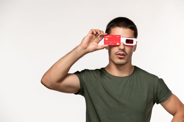 Vista frontal hombre joven en camiseta verde con tarjeta bancaria en gafas de sol d en película de pared blanca película de cine solitario masculino