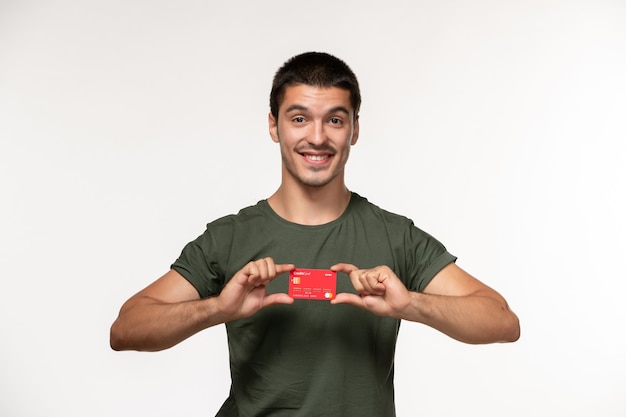 Vista frontal del hombre joven en camiseta verde con tarjeta bancaria en la película de pared blanca cine solitario