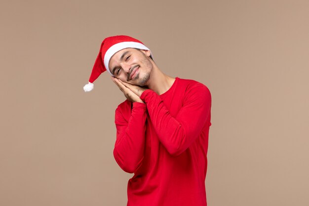 Vista frontal hombre joven cansado y tratando de dormir sobre fondo marrón emoción vacaciones de navidad