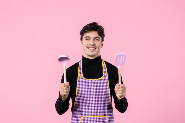 Vista frontal hombre joven en capa con cucharas sobre fondo rosa color comida cocina profesión uniforme masa horizontal cocina