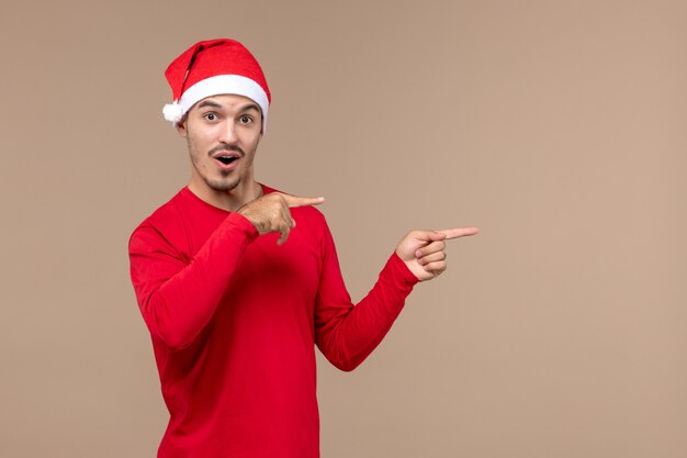Vista frontal del hombre joven con capa de Navidad sobre fondo marrón emoción vacaciones de Navidad