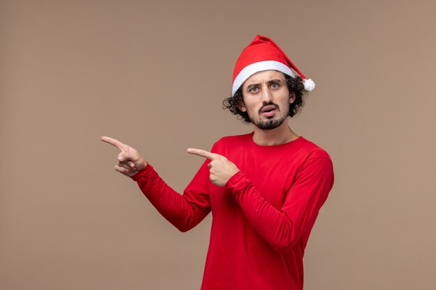 Vista frontal hombre joven con capa roja sobre fondo marrón emociones vacaciones navidad