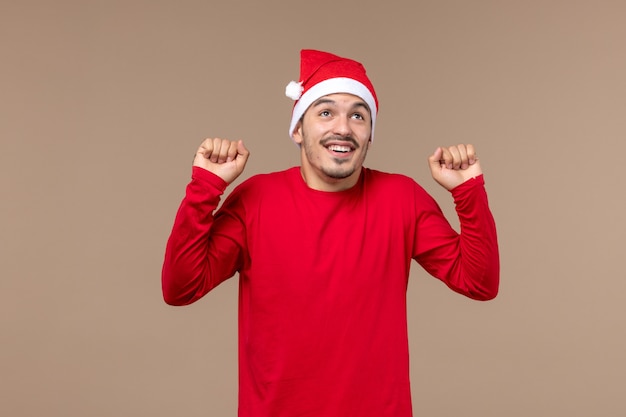 Vista frontal del hombre joven con cara emocionada sobre fondo marrón Navidad emociones vacaciones masculino