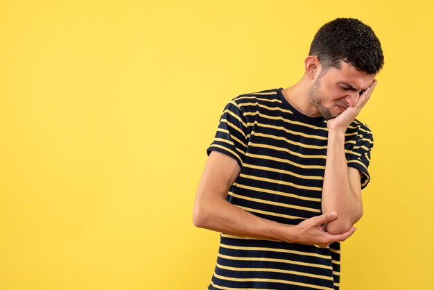 Vista frontal hombre joven decepcionado en camiseta a rayas blanco y negro fondo amarillo aislado