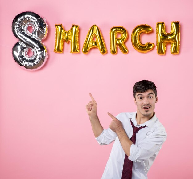 Vista frontal hombre joven con decoración de marzo sobre color de fondo rosa presente igualdad matrimonio femenino día de la mujer hombre