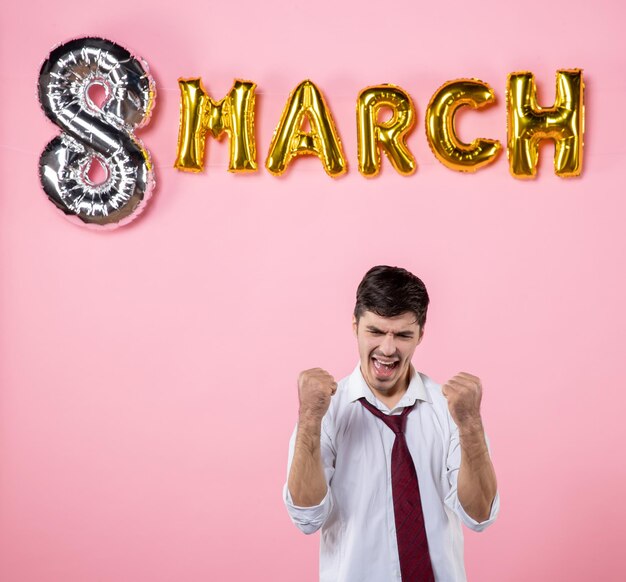 Vista frontal hombre joven con decoración de marzo sobre fondo rosa color igualdad matrimonio femenino día de la mujer hombre fiesta presenta