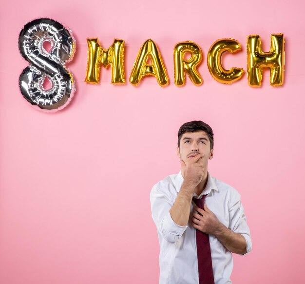 Vista frontal hombre joven con decoración de marzo sobre fondo rosa color matrimonio femenino día de la mujer presente hombre marido fiesta igualdad