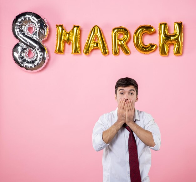 Vista frontal hombre joven con decoración de marzo sobre fondo rosa color matrimonio igualdad femenina día de la mujer fiesta presente hombre marido