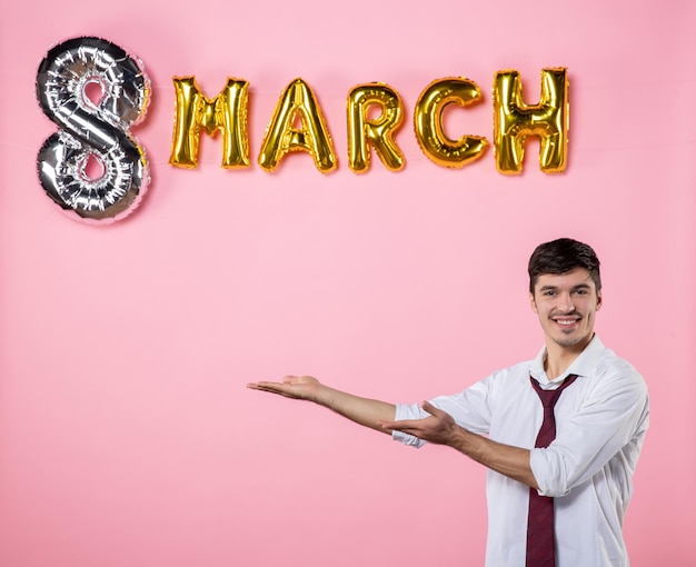 Vista frontal hombre joven con decoración de marzo sobre fondo rosa fiesta igualdad femenina día de la mujer presenta color matrimonio hombre