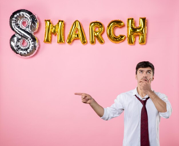 Vista frontal hombre joven con decoración de marzo sobre fondo rosa fiesta igualdad hombre femenino día de la mujer matrimonio colores presentes