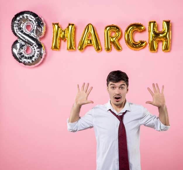 Vista frontal hombre joven con decoración de marzo sobre fondo rosa hombre matrimonio femenino marido igualdad día de la mujer fiesta presente