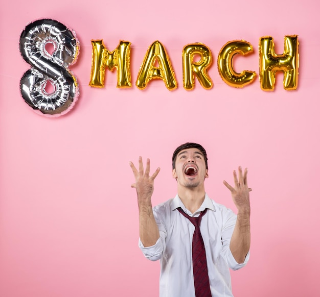 Vista frontal hombre joven con decoración de marzo sobre fondo rosa igualdad de color matrimonio día de la mujer hombre presente fiesta femenina