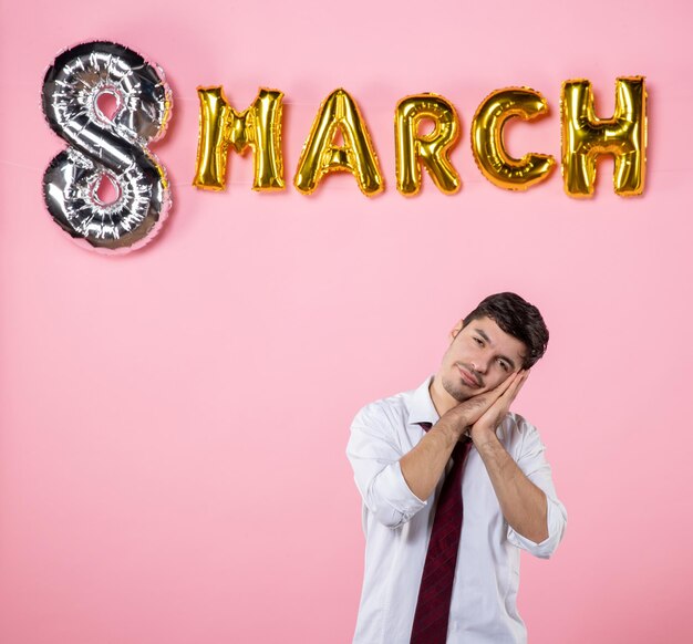 Vista frontal hombre joven con decoración de marzo sobre fondo rosa matrimonio femenino día de la mujer hombre marido fiesta igualdad presenta color