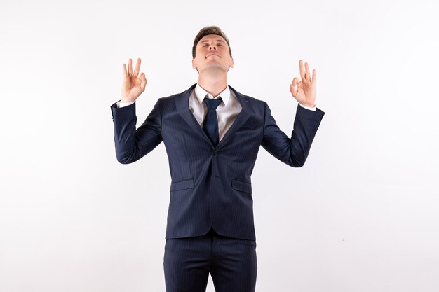 Vista frontal del hombre joven en elegante traje clásico en pose de meditación sobre fondo blanco.