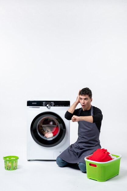Vista frontal del hombre joven esperando hasta el final del lavado de ropa en la pared blanca