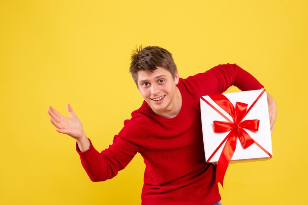 Vista frontal del hombre joven con gran Navidad presente en el escritorio amarillo