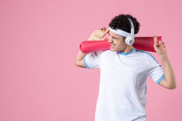 Vista frontal del hombre joven gritando en ropa deportiva con estera de yoga