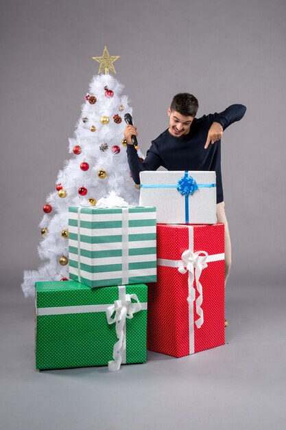 Vista frontal del hombre joven con micrófono y presenta en escritorio gris regalo de año nuevo navidad