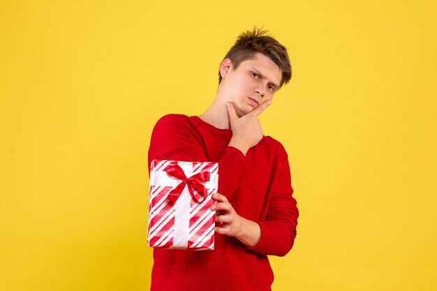 Vista frontal del hombre joven con Navidad presente sobre fondo amarillo
