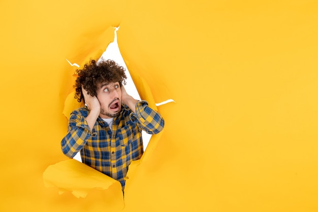 Vista frontal del hombre joven con el pelo rizado asustado sobre fondo amarillo rasgado