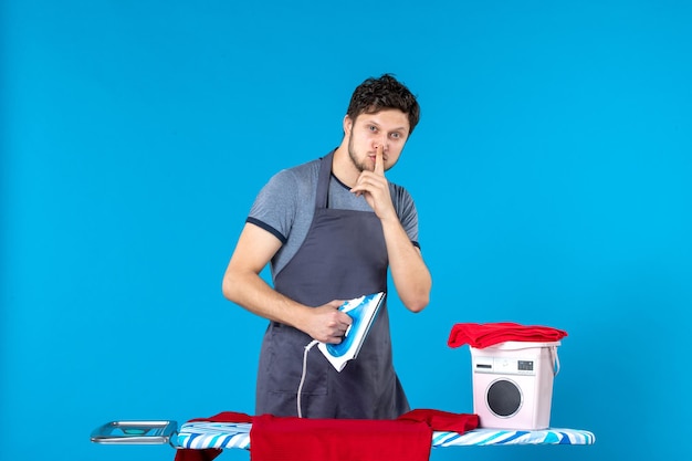 Foto gratuita vista frontal del hombre joven planchando la camisa roja sobre fondo azul lavandería iron man lavadora limpieza quehaceres domésticos colores