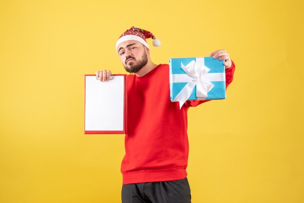 Vista frontal del hombre joven con presente de Navidad y nota sobre fondo amarillo