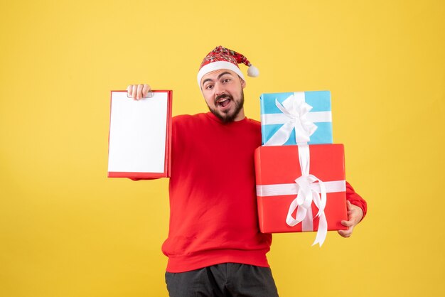 Vista frontal del hombre joven con presente de Navidad y nota sobre fondo amarillo